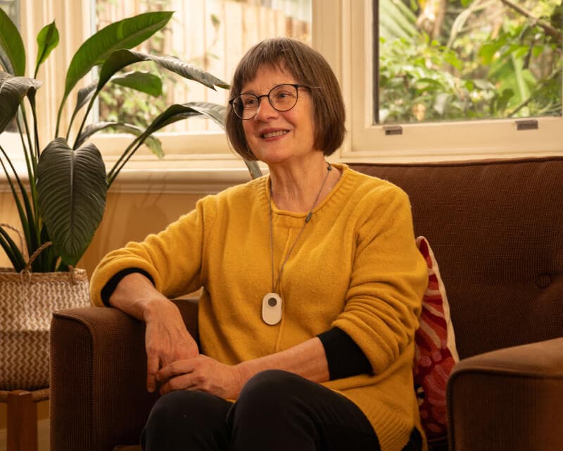 An older woman sitting in her lounge room wearing a Home Alarm pendant